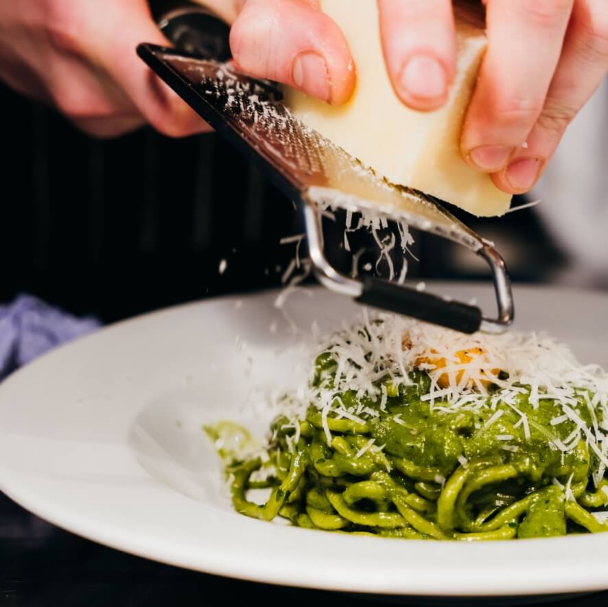 Cheese being grated onto pasta